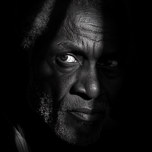 Old African man with wrinkled face in light and dark.