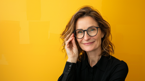 Smiling woman in black holds glasses on yellow background