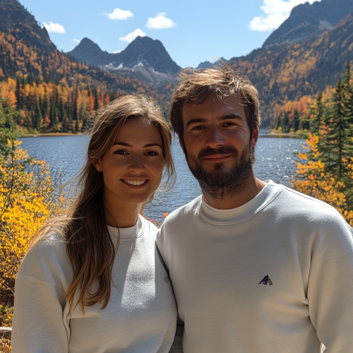 Two people smiling by lake and mountains.