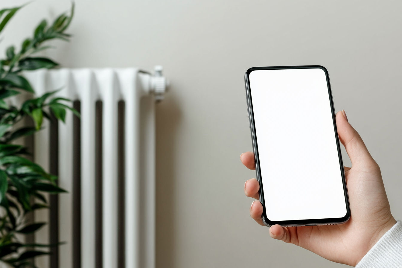 A hand holding phone near heating system