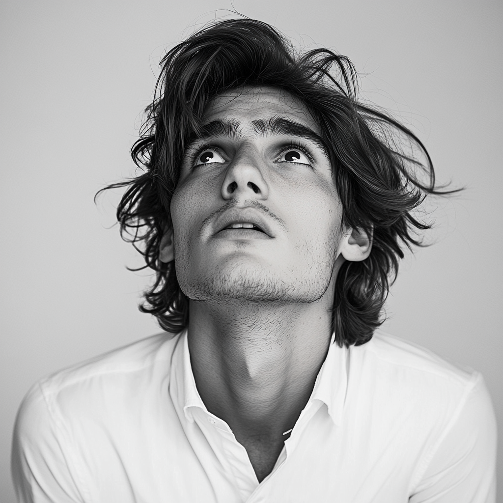 Frightened young man with long hair, white shirt, headshot.