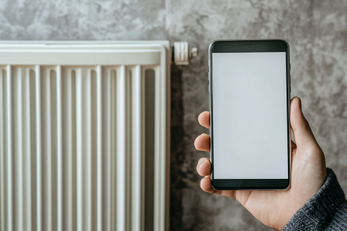 A hand holding phone near heating system