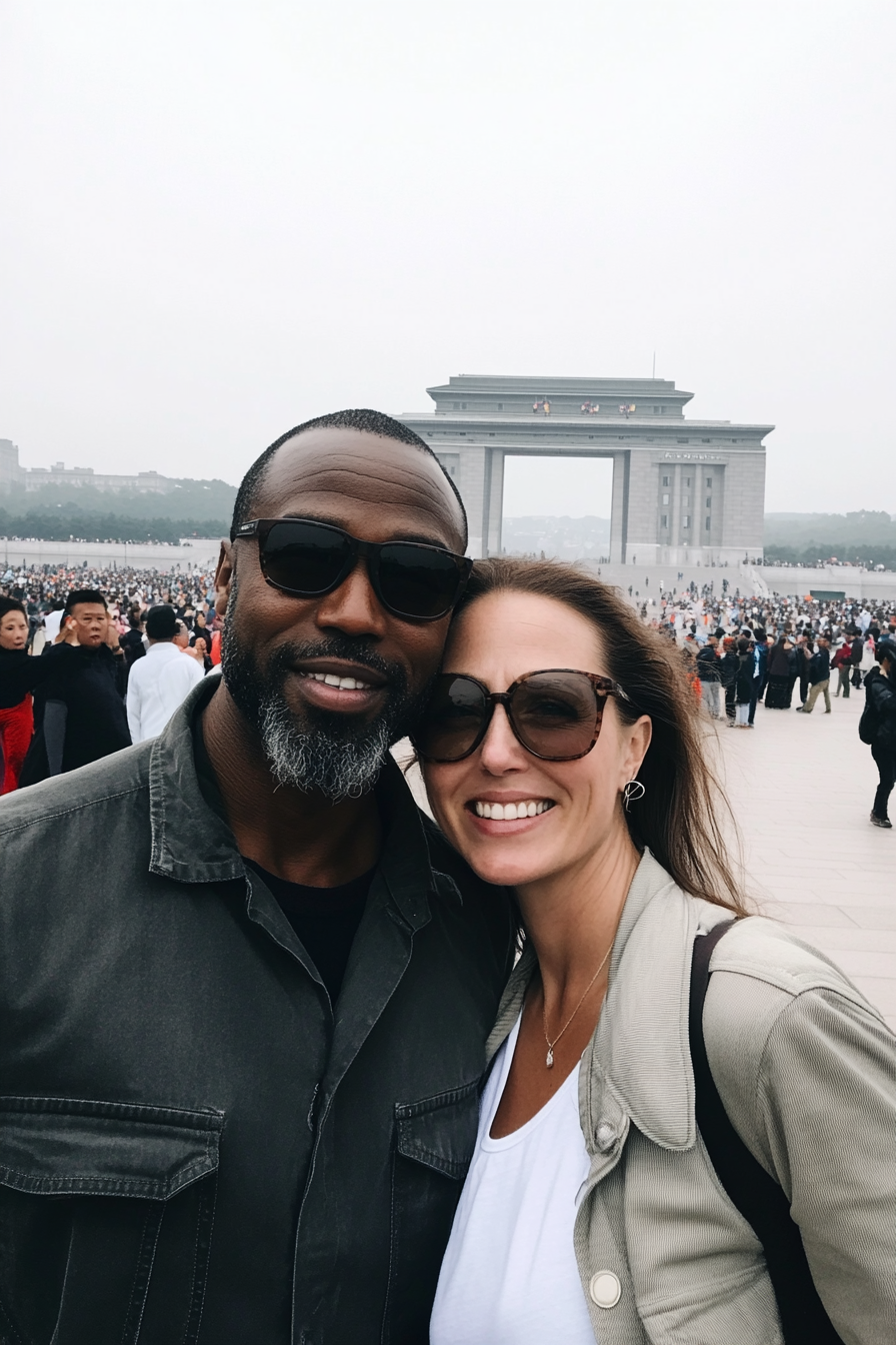 American couple at Reunification Arch with North Koreans in background.