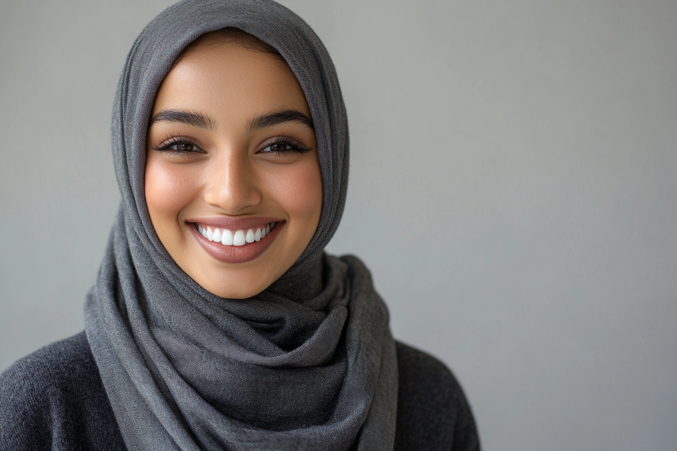 Beautiful hijabi woman in grey scarf, smiling at camera.