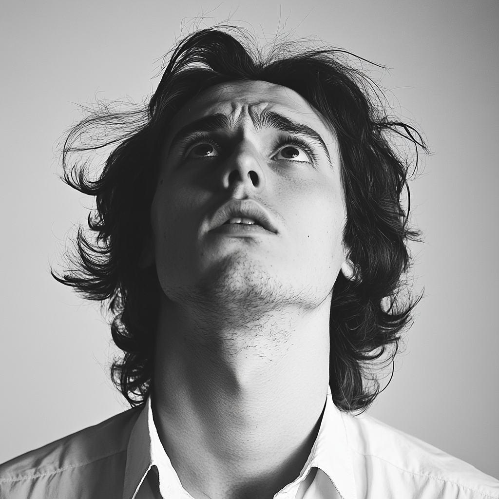 Frightened young man with long hair, white shirt, headshot.