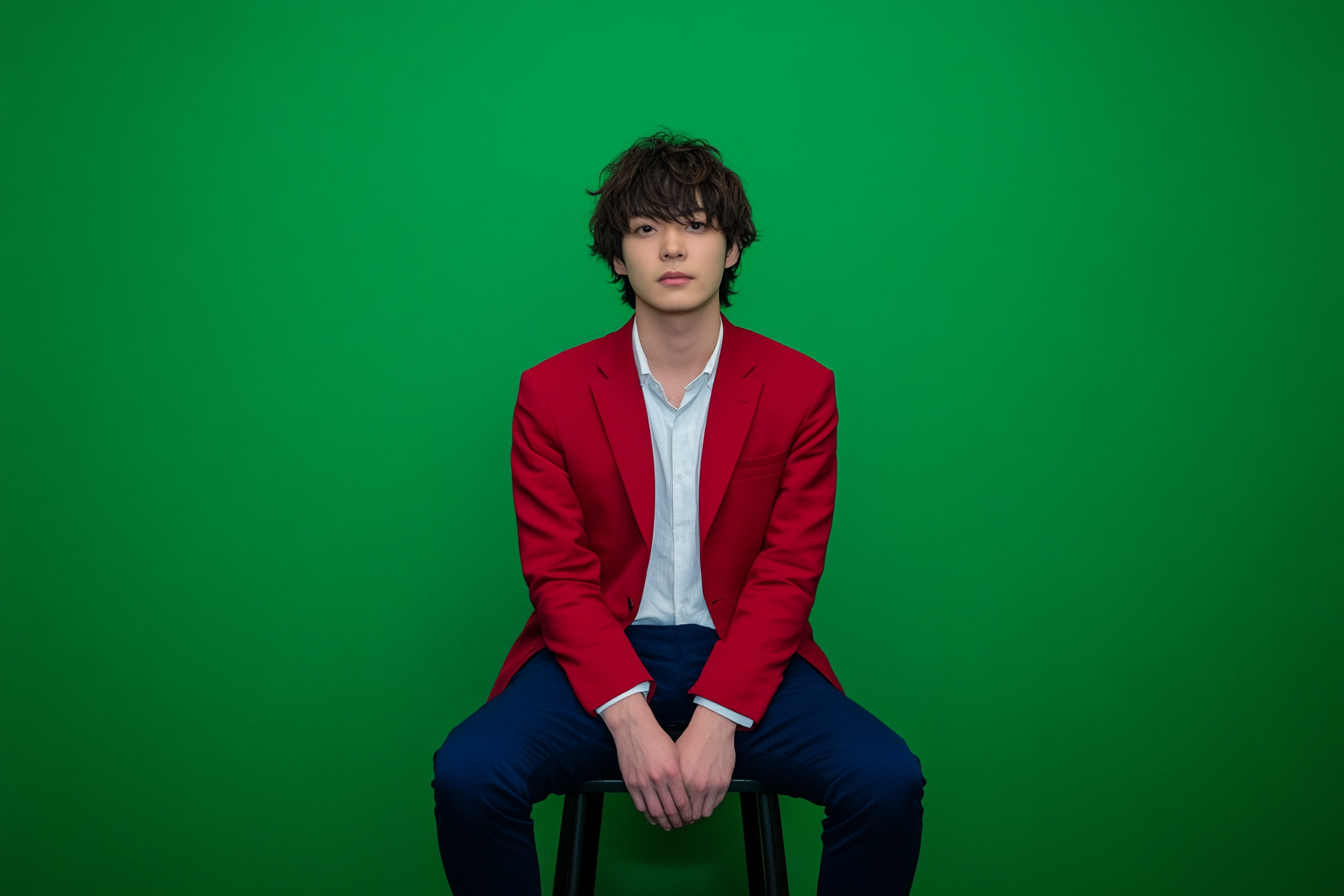 Japanese man in red blazer sitting on stool.